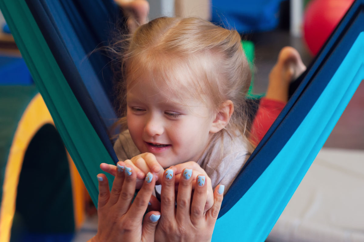 Girl enjoying a sensory therapy on a hammock while physiotherapist assisting her