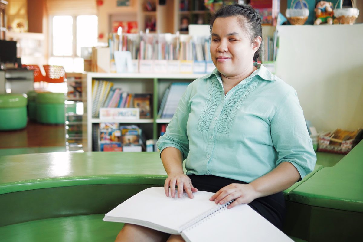 Young blind woman reading Braille book