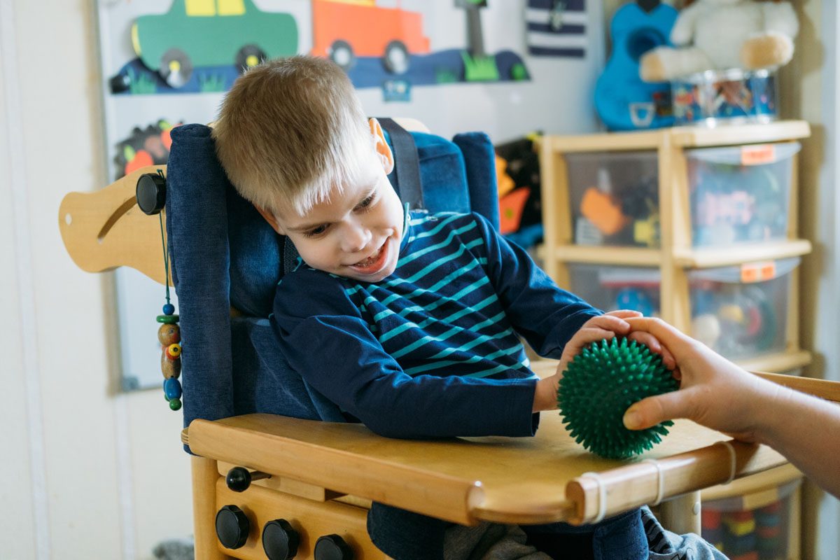 Boy with with Cerebral Palsy in special chair playing with sensory toy