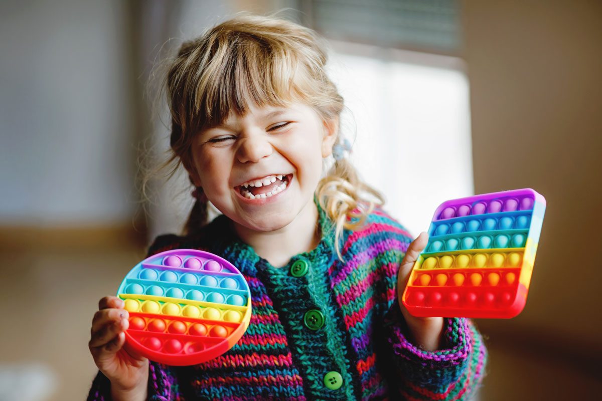 Preschool girl playing with new trend sensory toy - rainbow pop it.